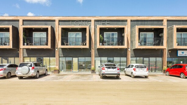 Un bâtiment moderne doté de nombreux balcons et d’un parking où sont garées plusieurs voitures.