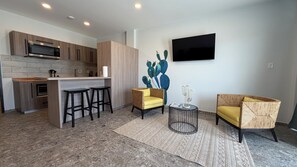 Una cocina moderna con microondas integrado, una zona de bar con taburetes, una obra de arte con cactus en la pared y un televisor de pantalla plana montado sobre el bar.