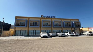 Un edificio de varios pisos con un letrero que dice 'LONG LIFE' y varios coches estacionados al frente.