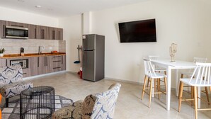Une cuisine moderne équipée d’un four à micro-ondes, d’un réfrigérateur et d’un coin repas avec des chaises blanches et une table.