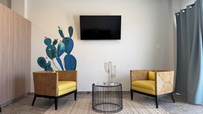 A modern living room with two wicker chairs, a round coffee table, and a cactus wall art piece. - Bushiri's Long Life Building-2BD/1BA APT-Sleeps 4 (Noord)