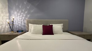 A hotel room with a bed, two bedside tables, a nightstand with a clock, and a wall with a textured design.