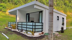 Una casa moderna d'una sola planta amb teulada plana, un porxo cobert i una petita zona de jardí amb diverses plantes i un camí.