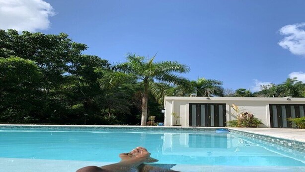 Vista a la piscina sota un cel clar, amb palmeres i un edifici modern al fons.