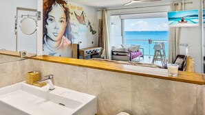 Un baño moderno con un lavabo grande, un espejo y vistas a un balcón con una cama y una mesa.