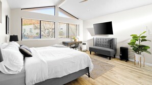 Ein modernes Schlafzimmer mit Bett, Schreibtisch, Stuhl, grauem Sofa, Fernseher und Deckenventilator.