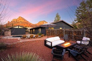 Relax in a tranquil outdoor space with a sofa, chairs, and fire pit, surrounded by a garden and scenic mountain views.