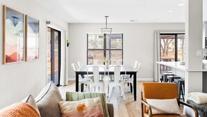 Ein modernes Wohnzimmer mit Essbereich, ausgestattet mit einem großen Fenster, einer Kristallleuchter und einer gemütlichen Sitzgruppe.