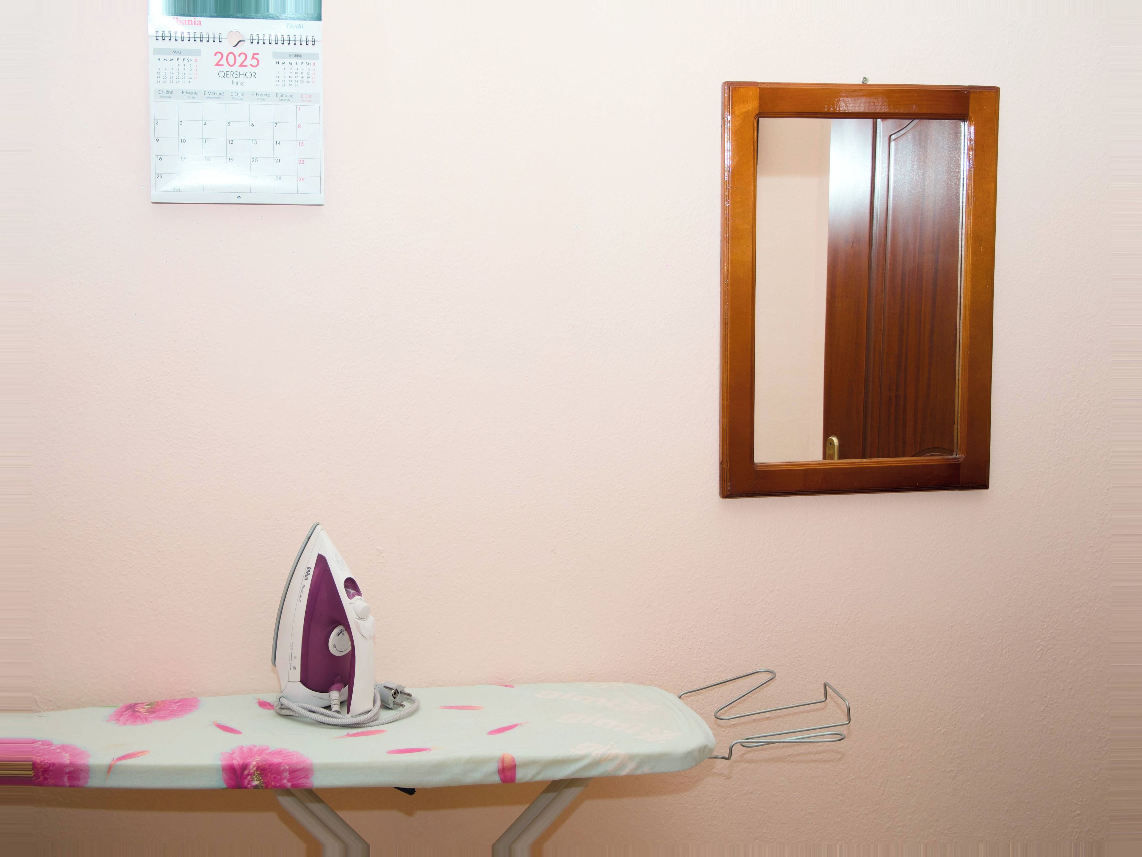 A room with a wooden-framed mirror, a wall calendar, and an ironing station.