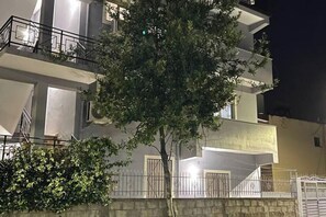 Un immeuble à plusieurs étages doté de balcons, avec un arbre au premier plan et un mur de pierre.