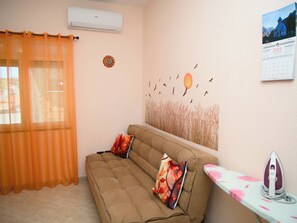 A room with a sofa, an ironing board, and a wall calendar.