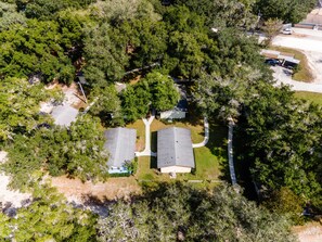 An aerial view of a residential area with two houses, surrounded by dense trees and a clear sky.
