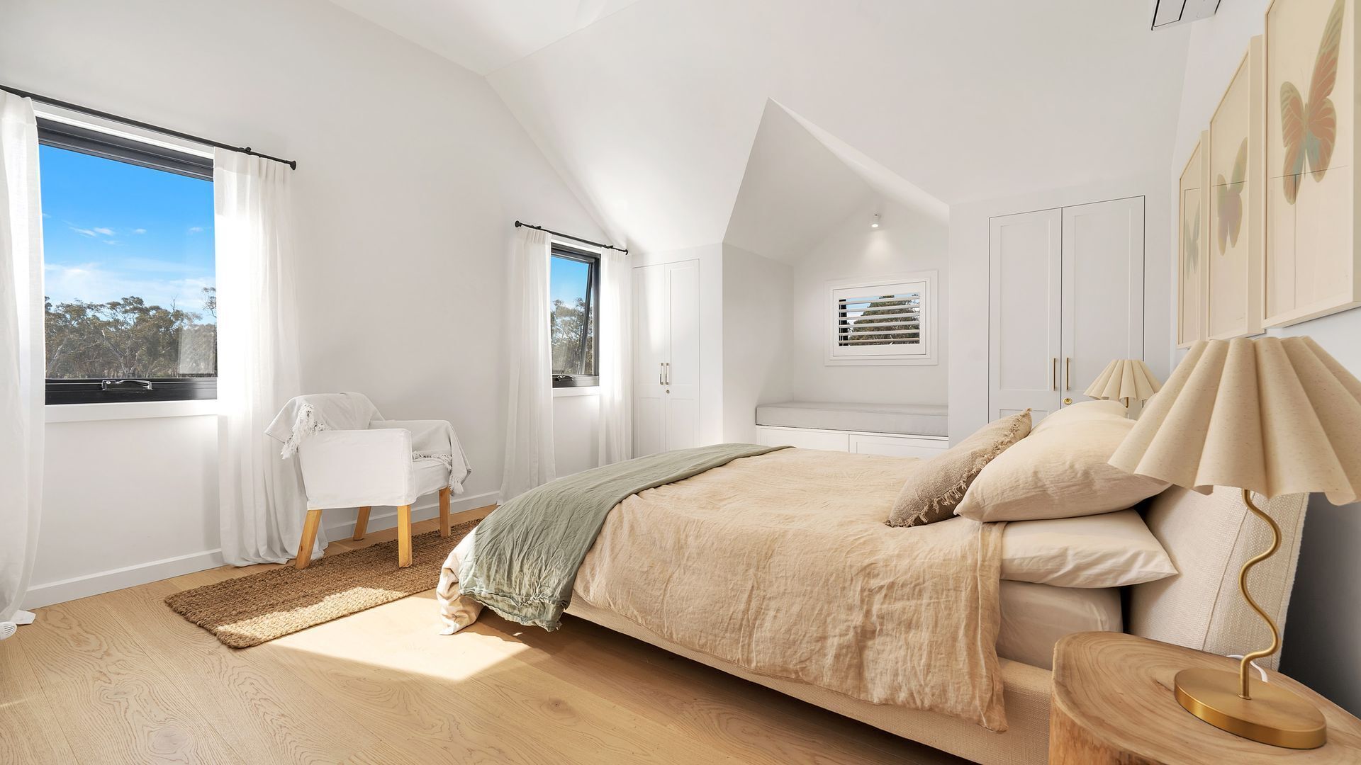 A bedroom with a large bed, a chair, a desk, and a window with curtains.