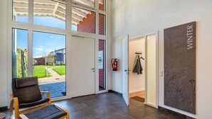 Une pièce spacieuse avec une grande fenêtre, une chaise, un porte-manteau et un mur sur lequel est affiché le mot « HIVER ».