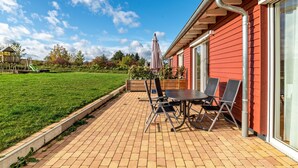 Une terrasse avec une table et des chaises, une plateforme en bois et un bâtiment rouge doté de grandes fenêtres.