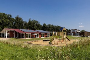 A building with a red roof and solar panels, a playground, and a grassy area with wildflowers. - Apartment 'Winter' with Shared Pool, Private Terrace and Wi-Fi (Straubenhardt)