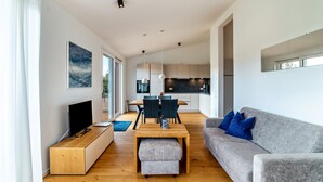 Un salon moderne doté d’un téléviseur à écran plat, d’une table basse en bois, d’un canapé gris agrémenté de coussins bleus et d’un coin repas avec une table et des chaises.