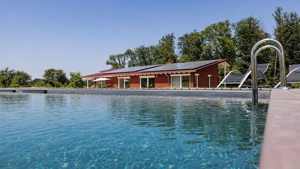 Una piscina con un edificio rojo al fondo, rodeada de árboles.