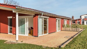 Un edificio rojo con un porche cubierto, grandes puertas correderas de vidrio y un camino de ladrillo que conduce a un área con césped.