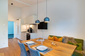 Una cocina moderna con comedor, mesa de madera, sillas y televisor montado en la pared.