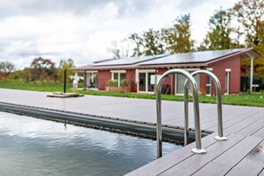 A swimming pool with metal railings, a red building in the background, and a grassy area. - Apartment 'Frühling' with Shared Pool, Shared Garden and Wi-Fi (Straubenhardt)