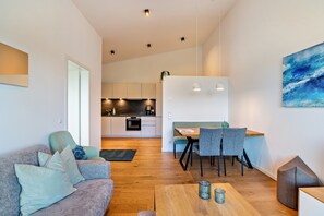 Ein modernes Wohnzimmer mit einer Couch, einem Esstisch mit Stühlen, einer Küche im Hintergrund und einem Bild an der Wand.
