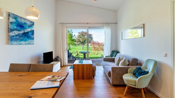 Een moderne woonkamer met een houten salontafel, een bank, een fauteuil en een schilderij aan de muur.