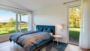 Slaapkamer met een groot bed, een klein nachtkastje en uitzicht op een tuin door een schuifdeur.
