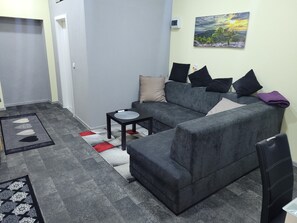 Un salon avec un canapé gris, une petite table noire et un tableau accroché au mur.