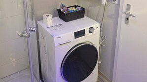 A compact laundry room with a front-loading washer and dryer, a small storage basket on the dryer, a towel rack above, and a shower area to the left. - Holiday Apartment " In Elz" with Wi-Fi (Elz)