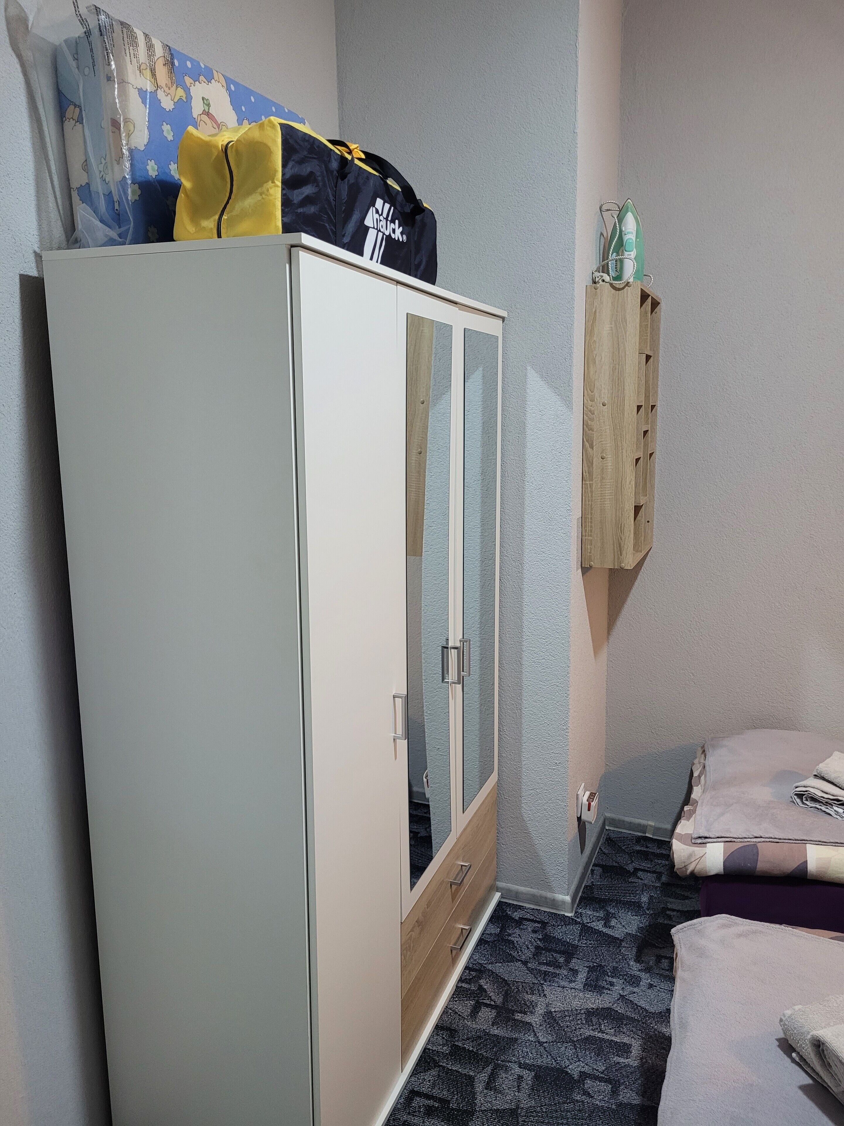 Une pièce comprenant une armoire, un lit, une étagère fixée au mur et un sol recouvert d’une moquette.