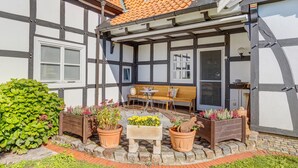 A traditional half-timbered house with a tiled roof, a wooden bench, a table, and potted plants. - Holiday Home 'Ferienwohnung Im Grünen' with Shared Terrace and Wi-Fi (Bissendorf)