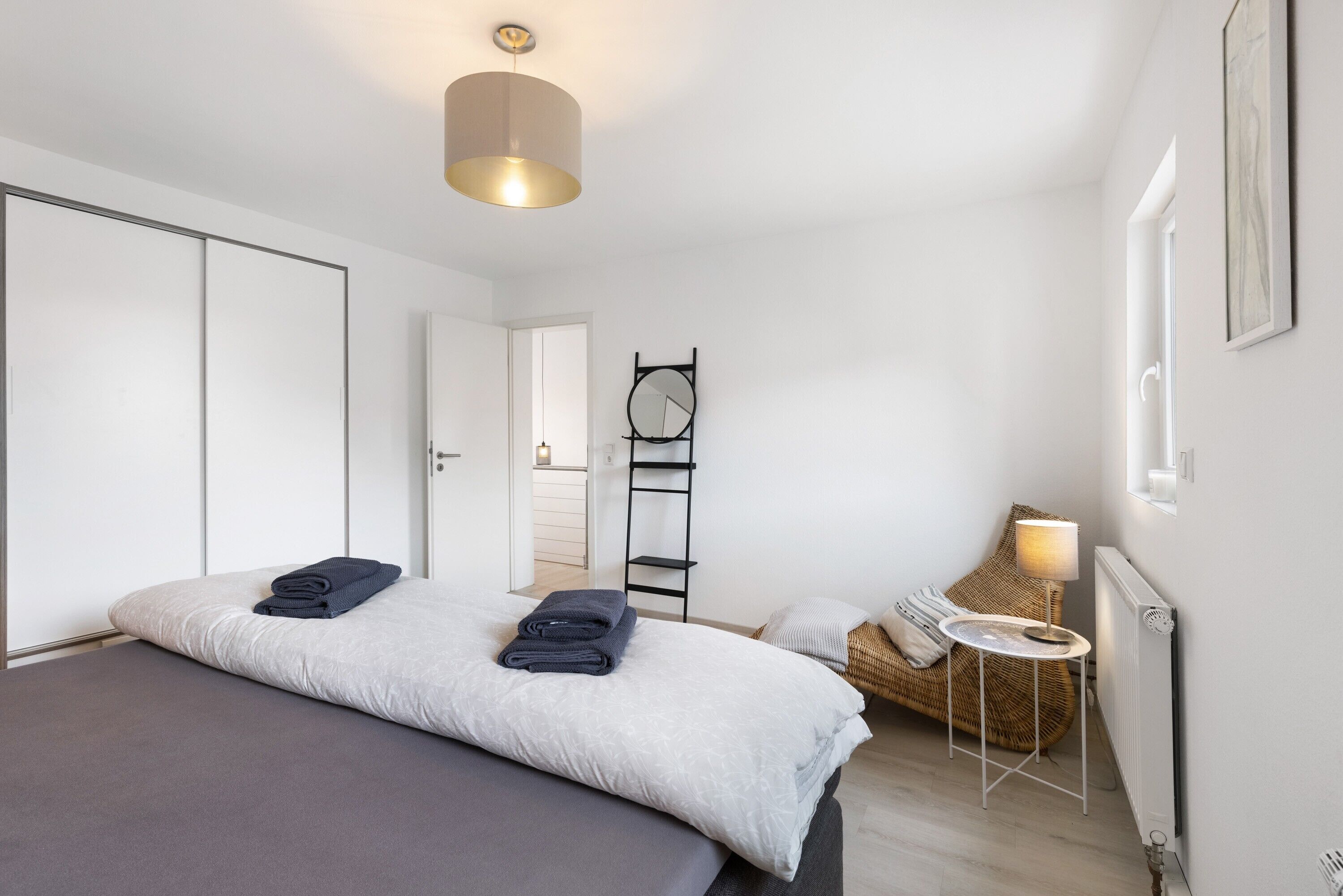 A bedroom with a bed, a bedside table, a lamp, a chair, and a ladder.