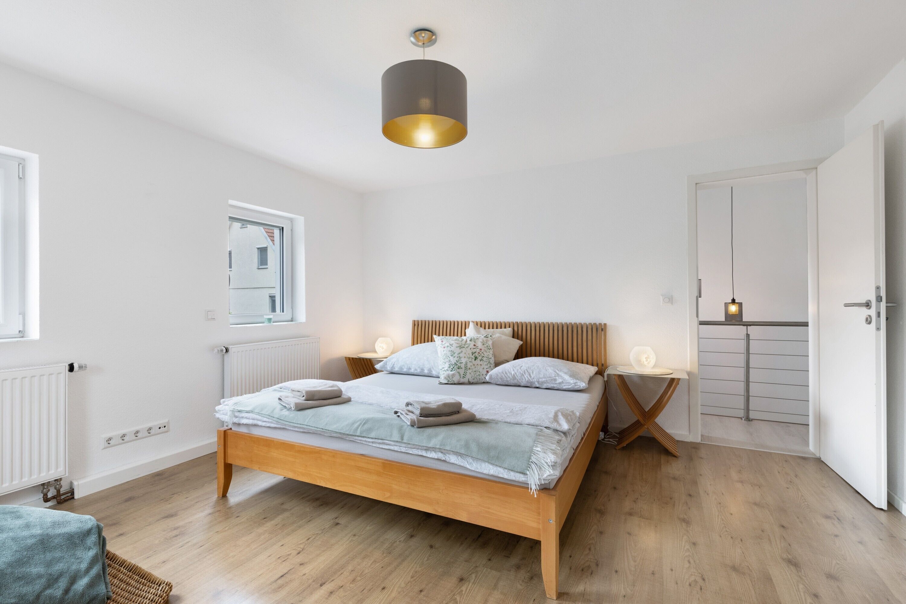 Una camera da letto con un letto di legno, comodini, una lampada a sospensione, un termosifone e una porta.