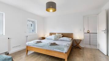 Una camera da letto con un letto di legno, comodini, una lampada a sospensione, un termosifone e una porta.
