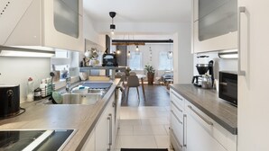 Une cuisine moderne équipée d’appareils électroménagers en acier inoxydable, un coin repas avec une table et des chaises, et une vue sur le salon.