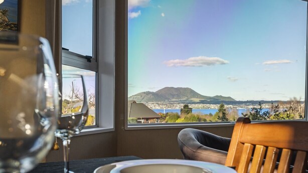 Ett matbord med tallrikar och ett vinglas, placerat framför ett fönster med utsikt över ett berg och en sjö.