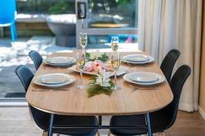 Mesa de comedor lista para cuatro personas, con platos, cubiertos y copas con un líquido transparente, probablemente vino, y un centro de mesa floral.