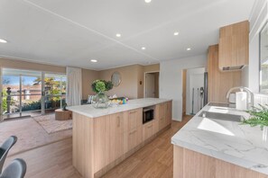 A modern kitchen with a central island, built-in oven, and a large window providing a view of the outdoors.