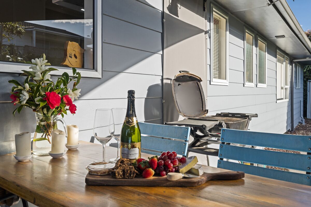 A dining table with a bottle of wine, glasses, a vase of flowers, and a variety of cheeses and fruits.