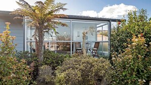 Ett modernt hus med en glasfasad, omgivet av olika växter och buskar.