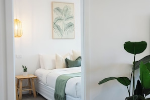 A bedroom with a bed, pillows, a bedside table with a plant, a hanging light, and a wall-mounted artwork. - Palm Stays | Ocean views | Space & style | Large family beach house (Vincentia)
