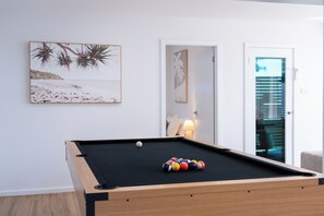 A pool table with balls, a framed picture of a beach, and a door leading to another room. - Palm Stays | Ocean views | Space & style | Large family beach house (Vincentia)
