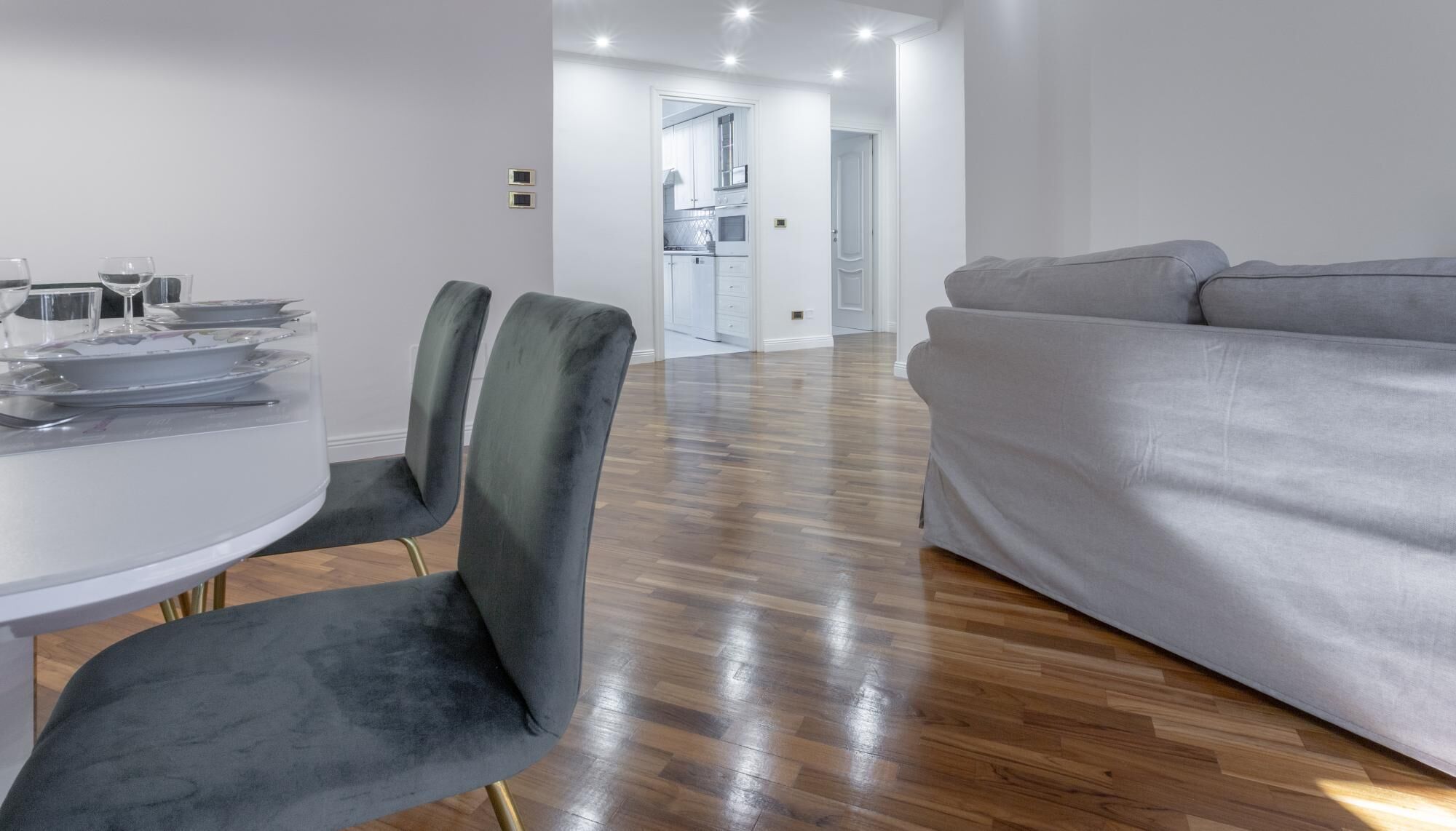 Una sala de estar moderna con un sofá gris, una mesa de comedor con sillas y una cocina al fondo.
