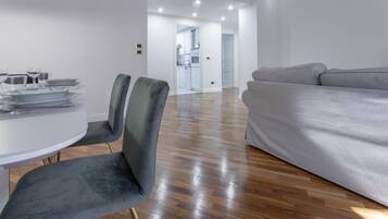 Una sala de estar moderna con un sofá gris, una mesa de comedor con sillas y una cocina al fondo.