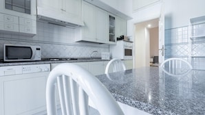 A modern kitchen with white cabinets, a granite countertop, a microwave, a dishwasher, and a dining area with a white chair. - Italianway Comfort - Bodio 6 (Milan)