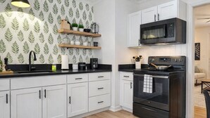 A modern kitchen with white cabinets, a black countertop, a microwave, an oven, and a striped rug.