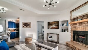 A modern living room with a fireplace, a dining area, and a kitchen visible through an open door.