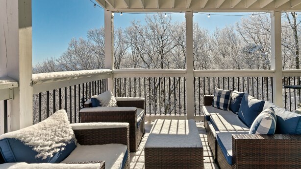 A covered outdoor seating area with wicker furniture and cushions, overlooking a snowy landscape.