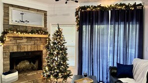 A living room with a stone fireplace, a Christmas tree, a dark blue curtain, and a modern ceiling light fixture.